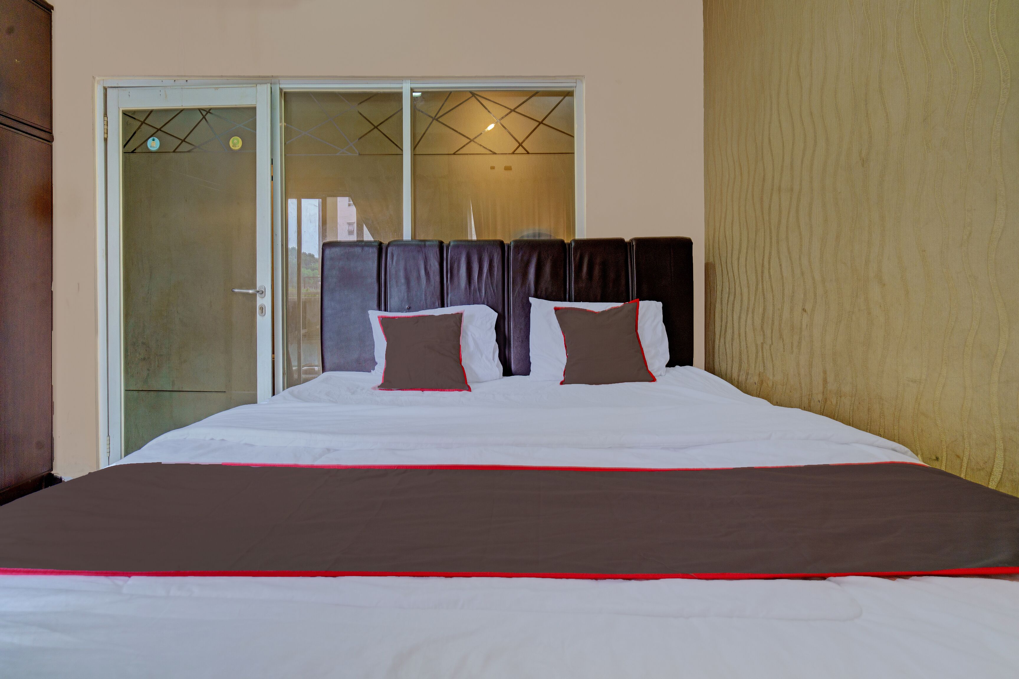 A hotel room with a large bed, a sliding glass door, and a wooden headboard.