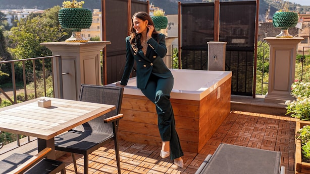 A terrace with a wooden table and chairs, a hot tub, and a view of a hillside. - Palazzo Martinelli  (Sorrento)