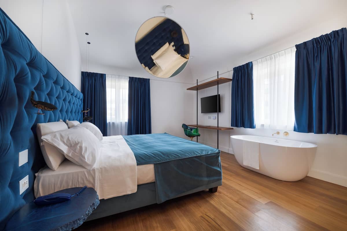Un dormitorio moderno con una cama grande, una bañera integrada y un espejo amplio.