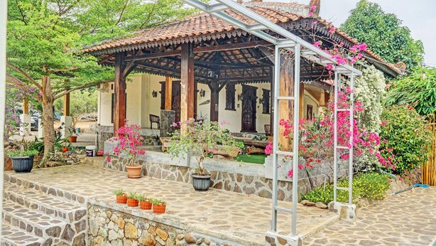 A covered patio area with stone flooring, potted plants, and a pergola structure.