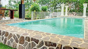 A rectangular swimming pool with stone walls and a white fence.