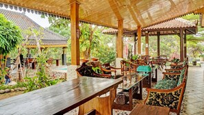 A covered outdoor dining area with wooden furniture and a tiled floor.