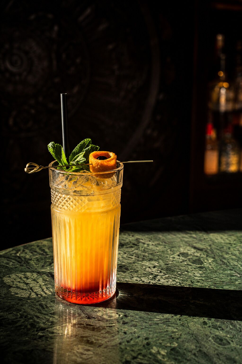 Um cocktail com canudo e guarnição num copo texturizado sobre uma superfície texturizada.