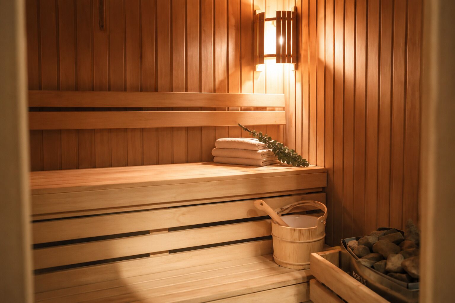 A sauna with wooden benches, a towel stack, a bucket, and a container of stones.