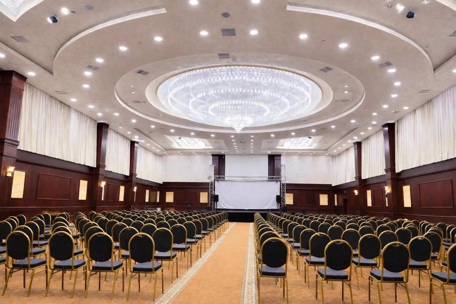 A conference room with rows of chairs, a large screen, and a chandelier.