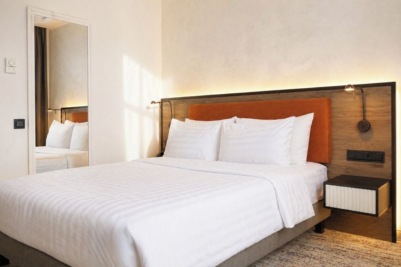 Une chambre d’hôtel avec un grand lit, une table de chevet, une lampe fixée au mur et un miroir.