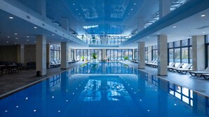 A large indoor swimming pool with clear glass walls, sun loungers, and a high ceiling. - Eighty Eight Hotel and Spa (Tsaghkadzor)