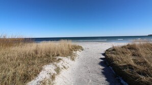 Ein sandiger Küstenpfad führt zum Meer, gesäumt von hohem Gras.
