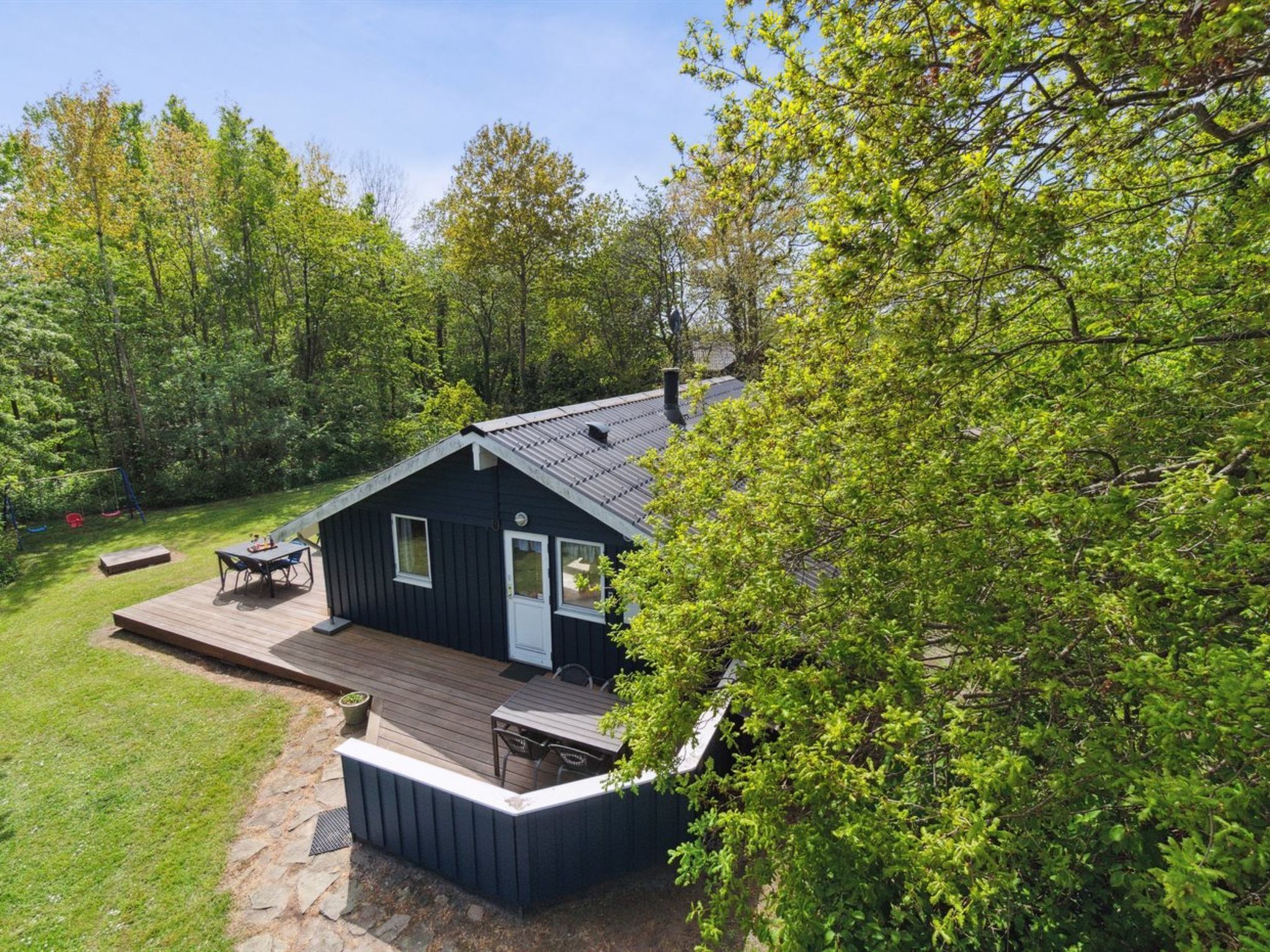 En stuga med en veranda, en liten sittplats utomhus och utsikt över den omgivande skogen.