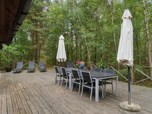 Terraza exterior con mesa y sillas, rodeada de árboles.