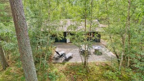 Un chalet isolé, entouré d’une forêt dense, doté d’une terrasse en bois et d’un espace salon extérieur.
