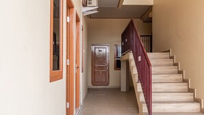 A hallway with a wooden door labeled 104, a staircase with a red handrail, and a tiled floor. - Hotel O Alnasya Syariah (Palembang)