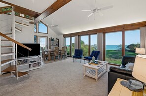 A spacious living area with a staircase, a flat-screen TV, a dining table, and chairs.
