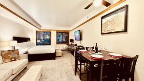 A hotel room with a bed, a desk, a dining table set for two, a TV, and a framed map on the wall. - Slopeside 2753a (Keystone)
