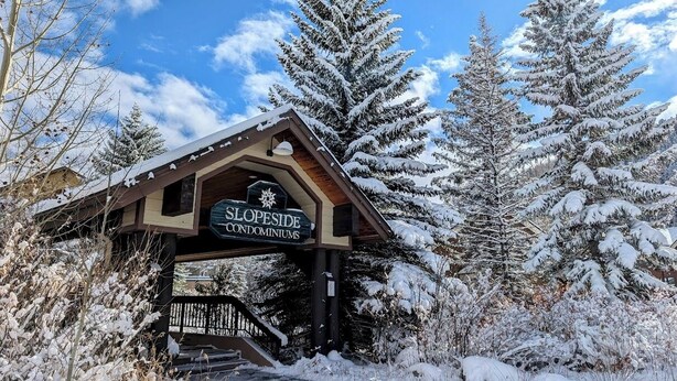 A wooden building with a sign reading "SLOPESIDE CONDOMINIUMS" in a snowy landscape. - Slopeside 2753a (Keystone)