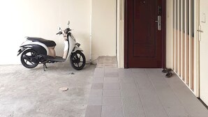 Un espace extérieur abrité où se trouve une trottinette garée près d’une porte.