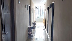 Un long couloir étroit, doté de carreaux au sol et de portes de part et d’autre.
