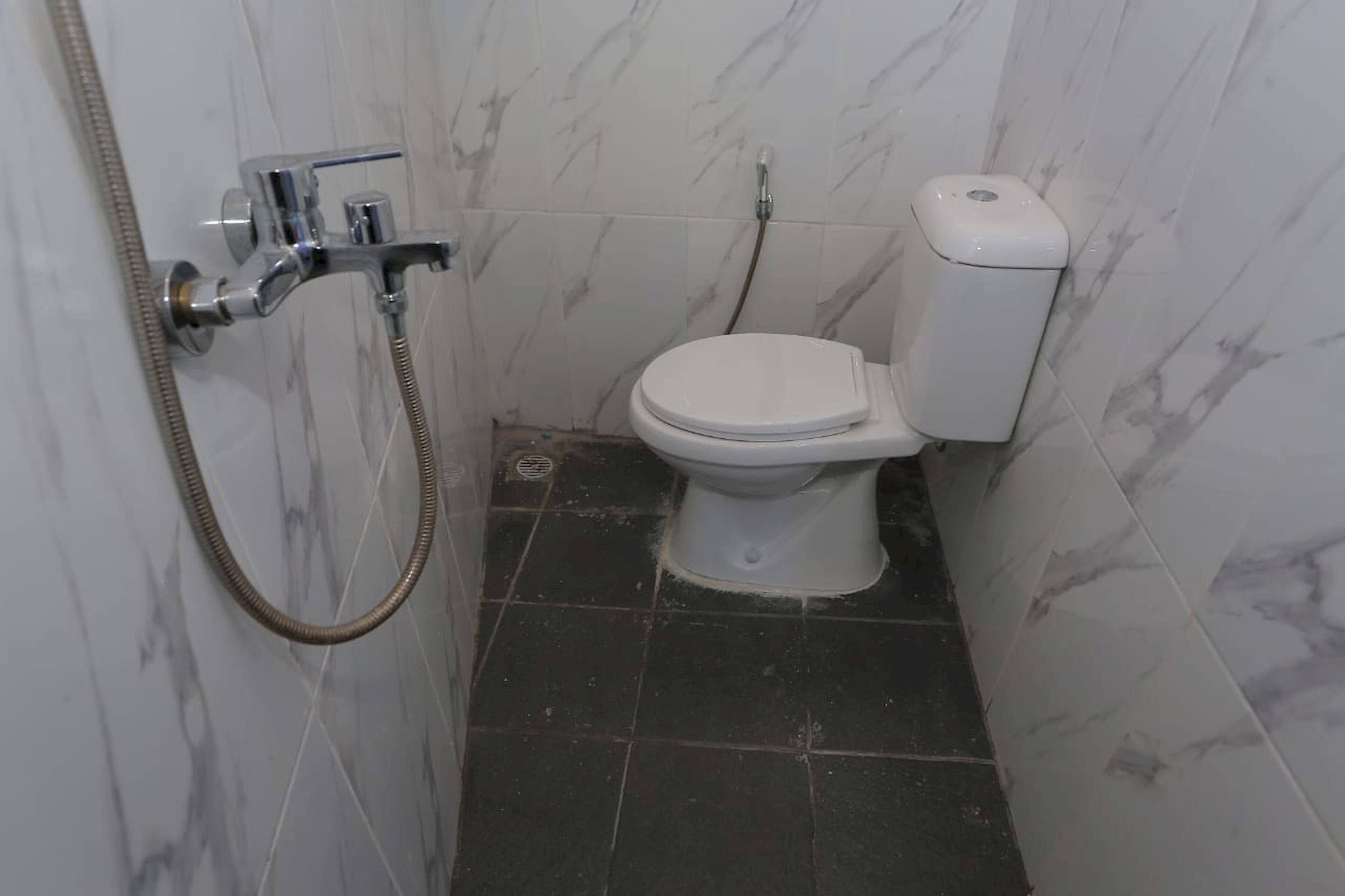 A small bathroom with a toilet, a shower, and a marble wall.