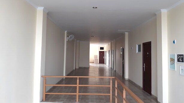 Un long couloir étroit, doté d’une rambarde en bois, de plusieurs portes et d’un ventilateur de plafond.