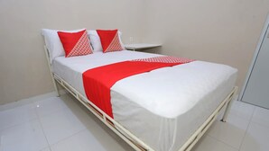 Un lit avec une literie blanche et des touches de rouge, une table de chevet et un mur sobre.