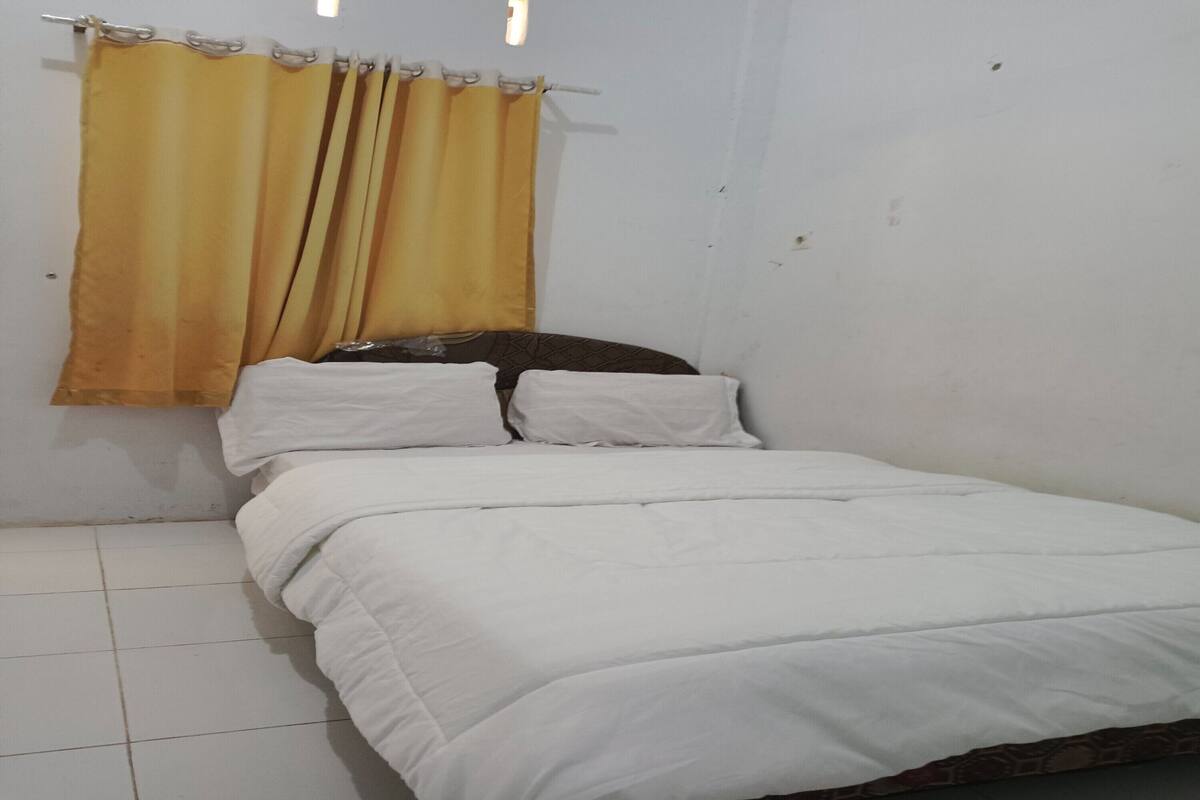 A single bed with white bedding, a wooden headboard, and a yellow curtain.