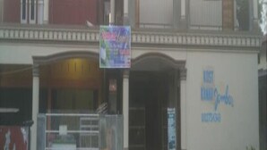 Un immeuble de deux étages avec un balcon au deuxième étage. Au premier étage, on peut lire une enseigne sur laquelle est écrit : « Kost Kafe Samba ».
