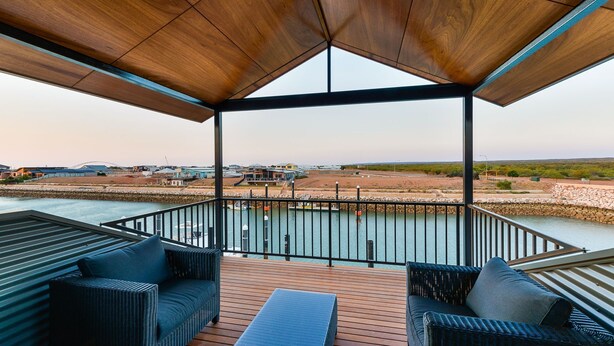 Una terraza techada al aire libre con mobiliario de mimbre y vistas a un río y edificios a la distancia.