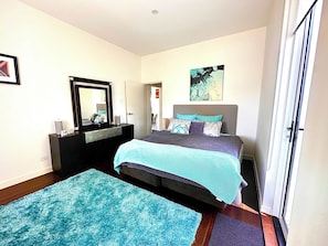 Une chambre à coucher avec un lit, une commode, un miroir, une porte et une fenêtre.
