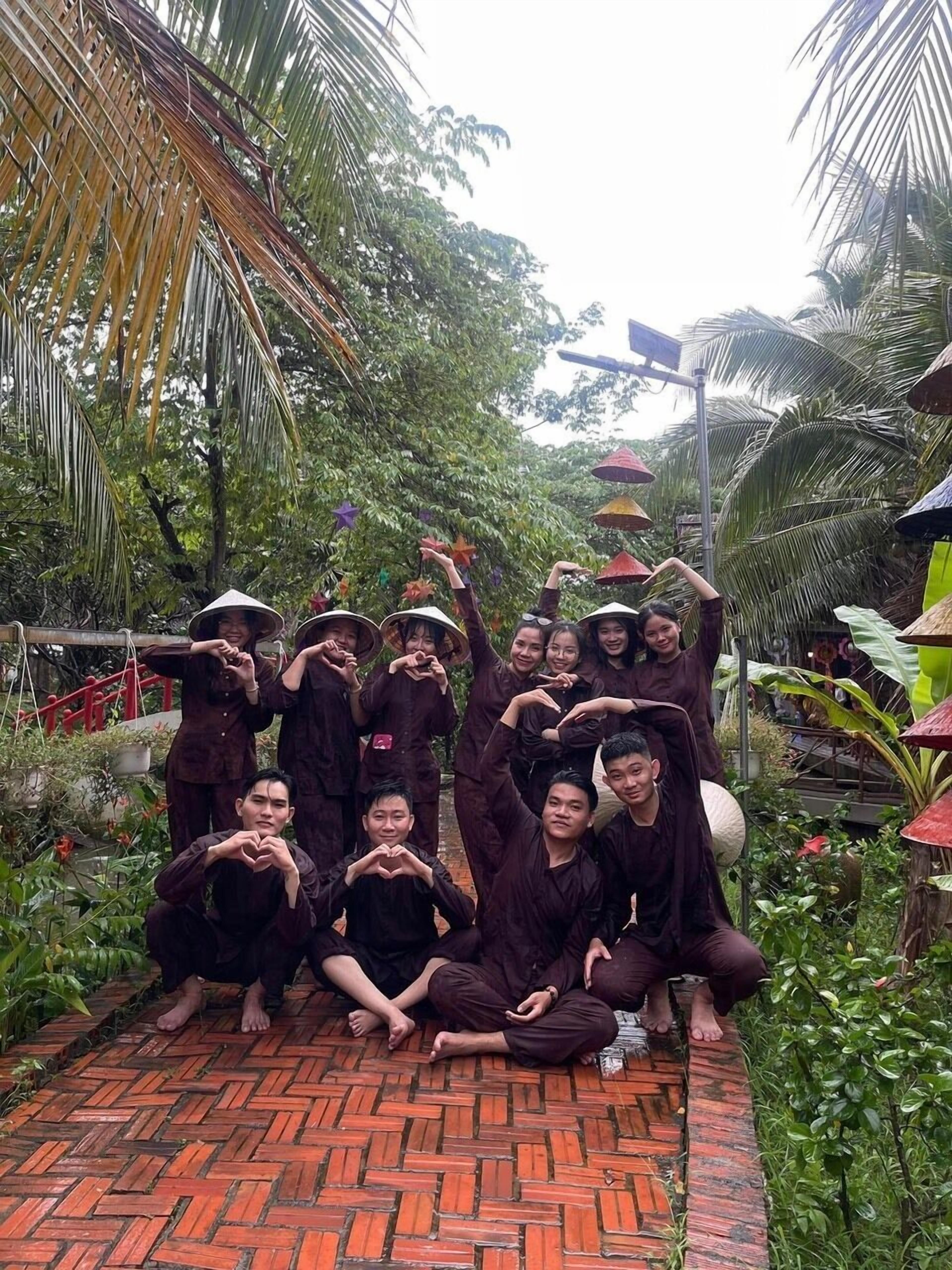 A group of people in traditional attire posing in a garden with a brick pathway and tropical vegetation.