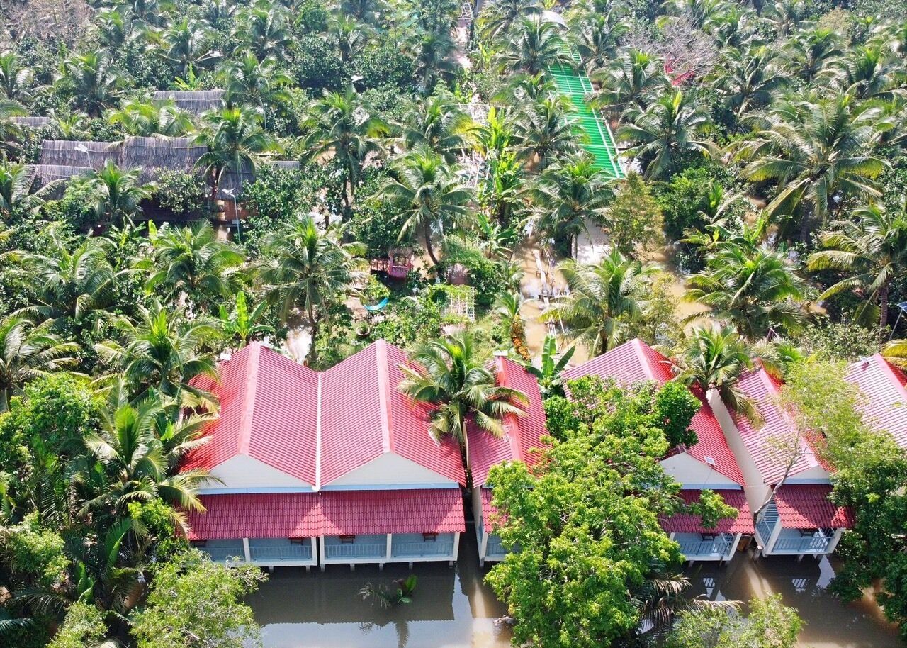 A cluster of red-roofed buildings surrounded by lush greenery and palm trees, indicating a tropical resort setting.