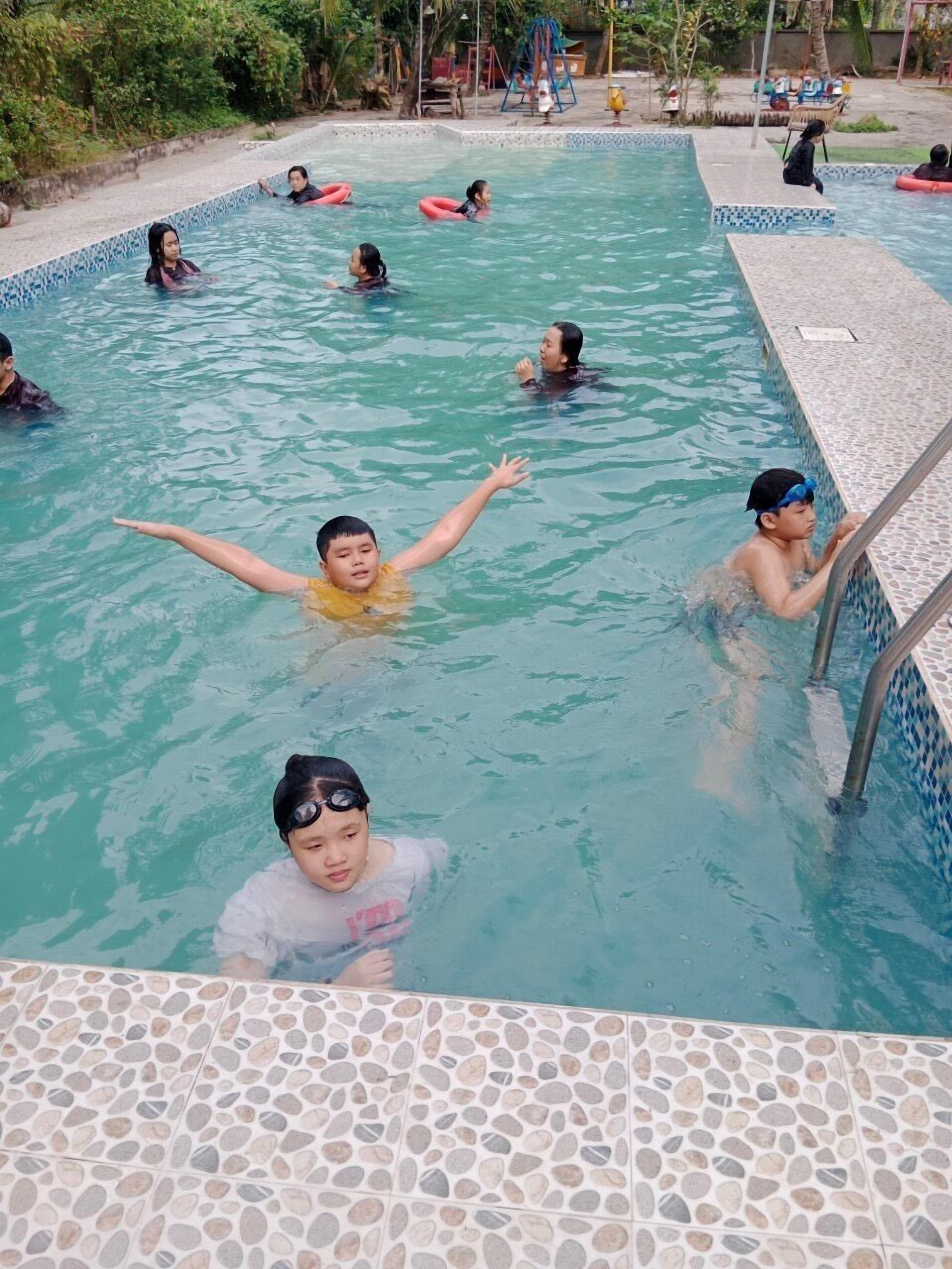 Una piscina con agua azul cristalina, bordes azulejados y suelo con diseño de guijarros.