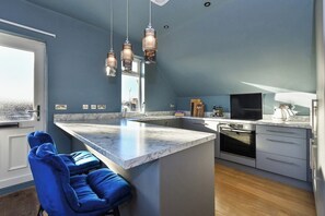 A modern kitchen with a marble island, pendant lights, and a built-in oven.