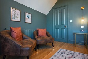 A room with two brown armchairs, a blue door, a small table with a radio, and framed botanical prints on the wall.