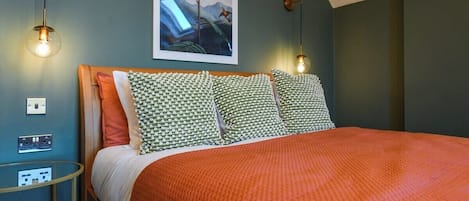 A bedroom with a bed, patterned pillows, a wall-mounted artwork, and a bedside table with a lamp.