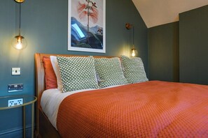 A bedroom with a bed, patterned pillows, a wall-mounted artwork, and a bedside table with a lamp.