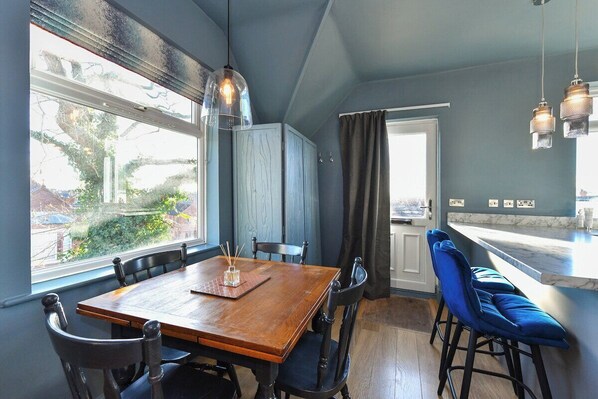 A dining area with a wooden table and chairs, a window with a view of greenery, and a kitchen area with a marble countertop.