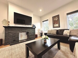 Una sala de estar con chimenea, un sofá, una mesa de centro y un televisor montado en la pared.