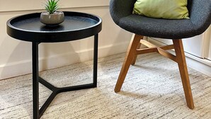 A room with a window, a small round table with a plant, and a modern chair with a cushion. - Luxury & Grandeur | Balcony Views| Prime Location, Parking (Hawthorn)