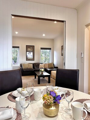 A dining area with a table set for four, a coffee table with a vase of flowers, and a view into a living room with a sofa and a window.