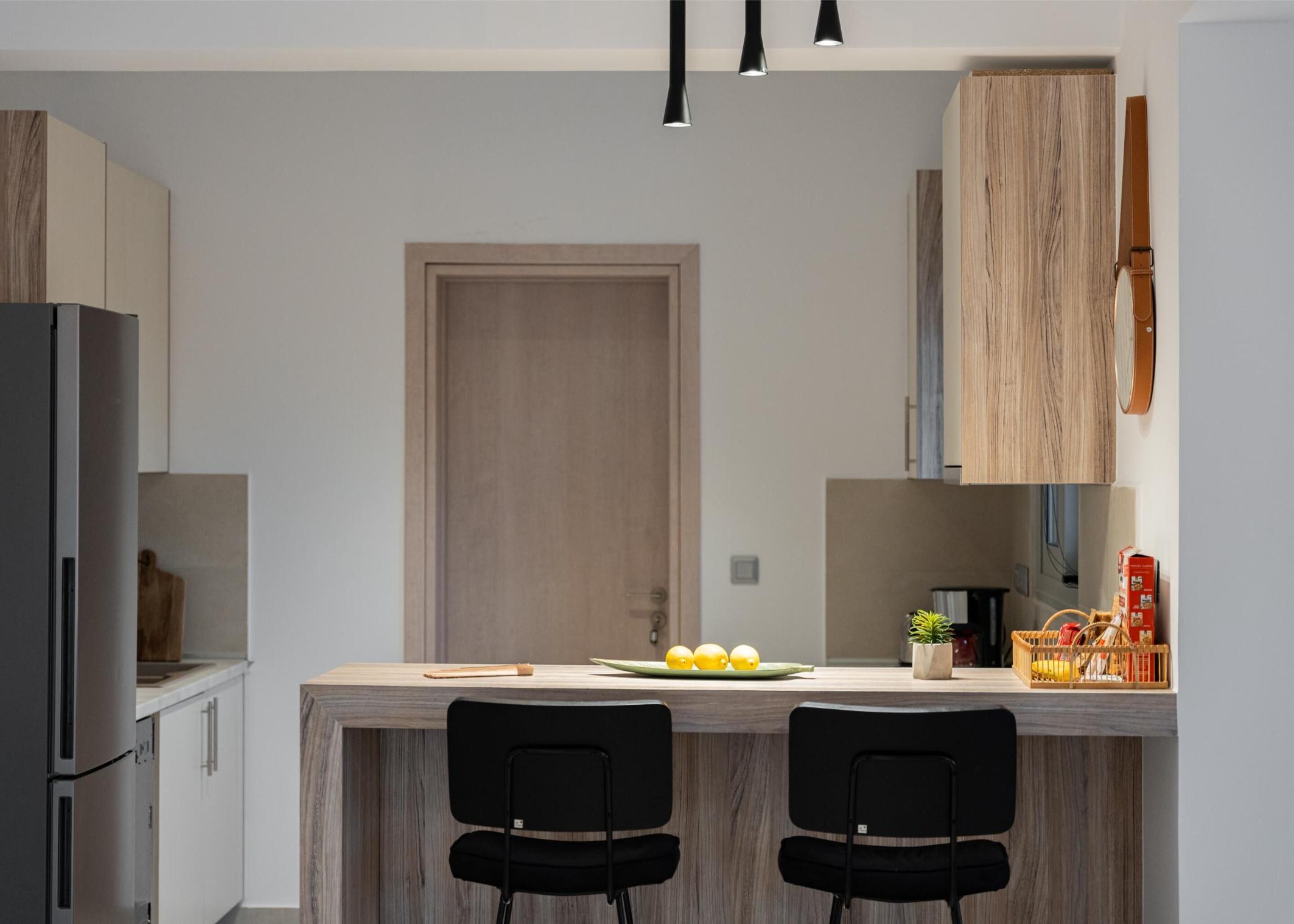 Una cocina moderna con una isla de madera, dos sillas negras, un refrigerador y un armario de madera.