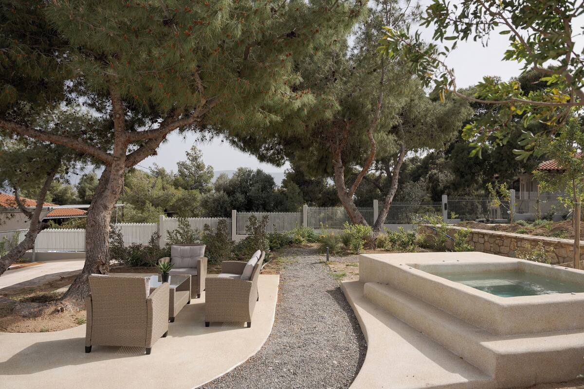 An outdoor patio area with wicker furniture, a concrete pool, and surrounding trees.