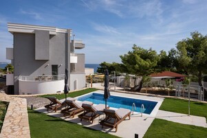 Un edificio moderno con zona de piscina, sillones de descanso y vistas despejadas al mar.