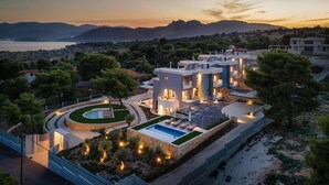 A modern villa with a swimming pool, surrounded by landscaped gardens and a view of the sea and mountains. - Cavos Boutique Homes (Corinth)