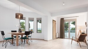 A spacious room with a large dining table, chairs, and a view of the outdoors through the windows. - Cavos Boutique Homes (Corinth)