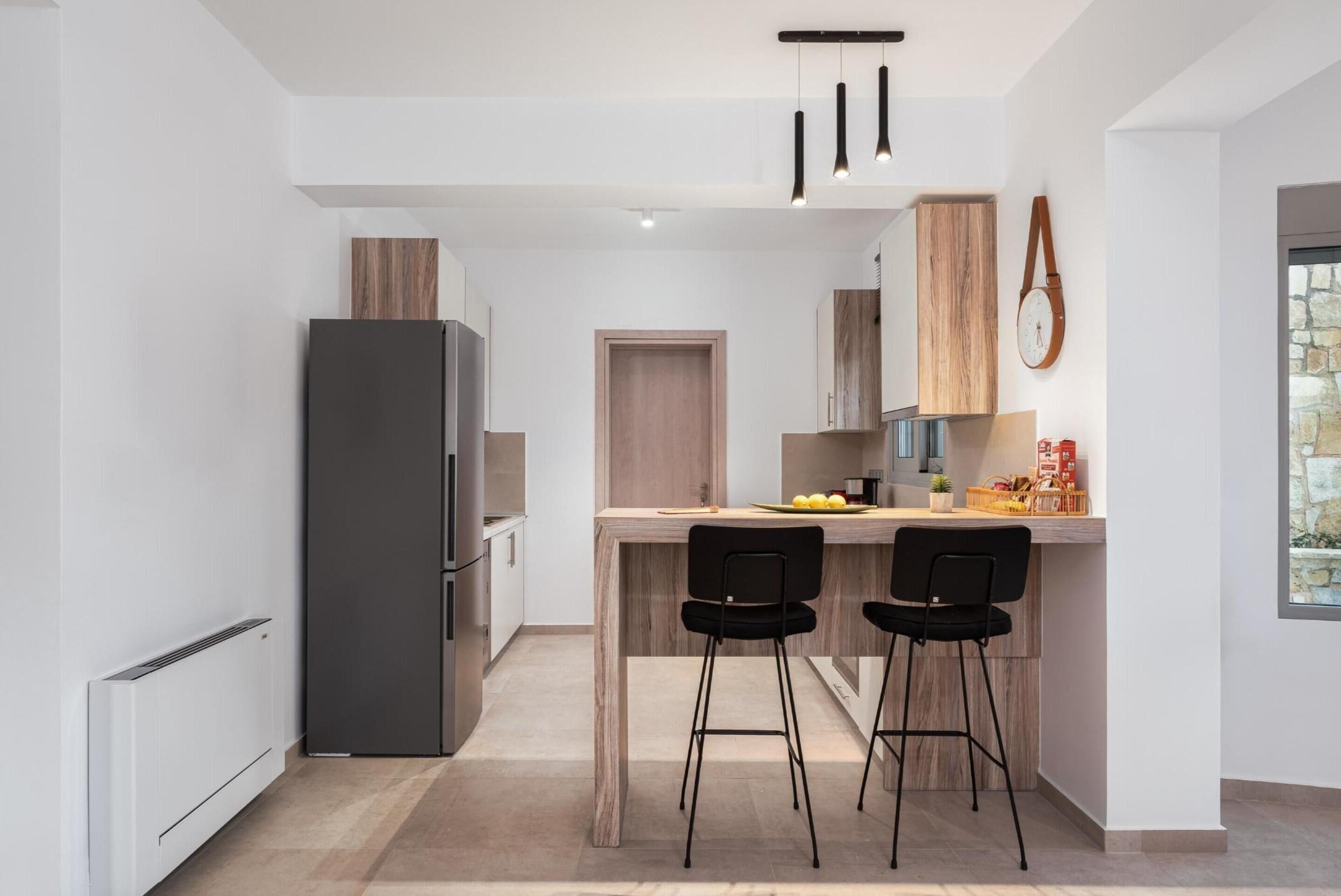 Cozinha moderna com uma ilha central, dois banquetes pretos, uma geladeira e armários de madeira.