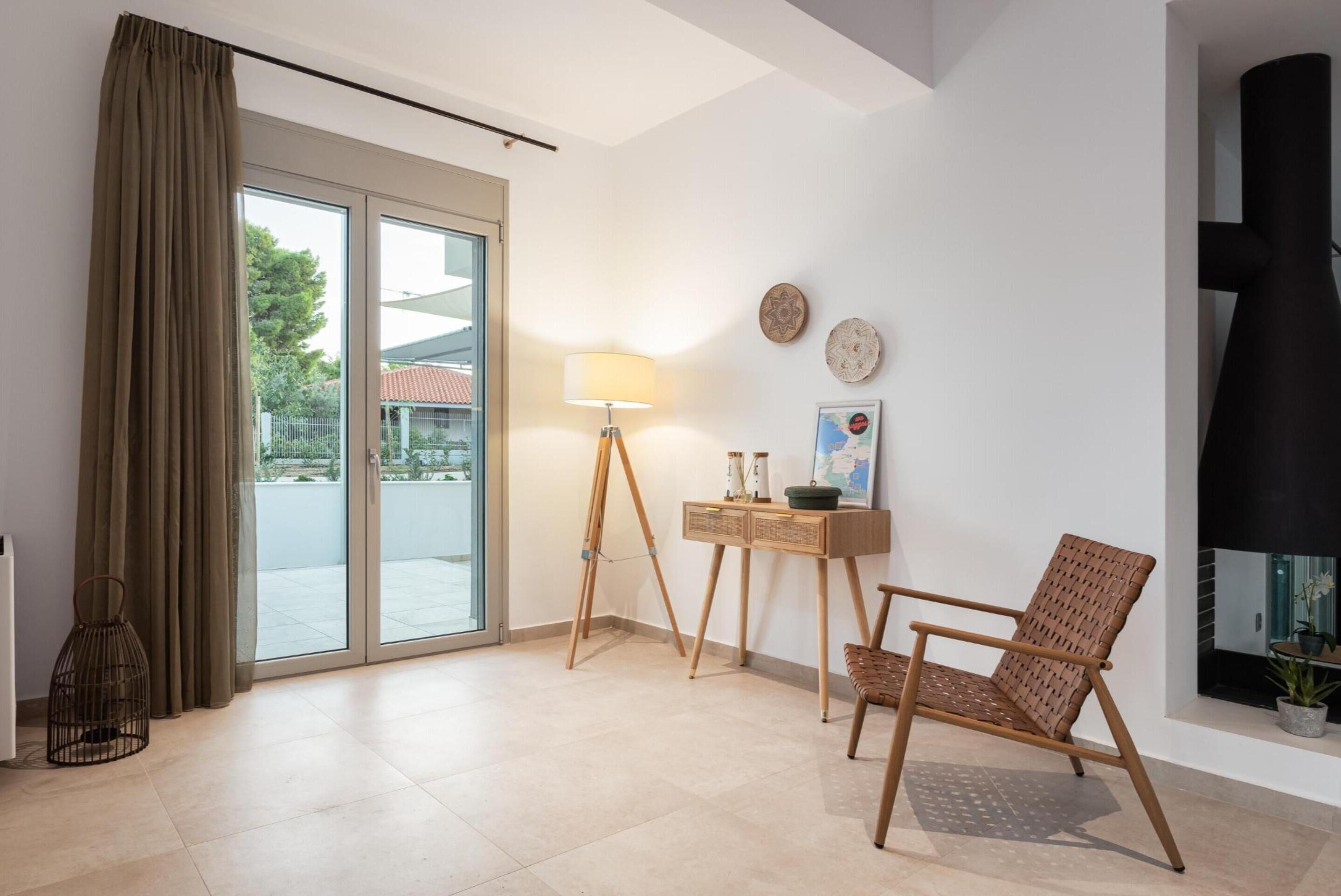 Una sala de estar moderna con un ventanal corredero, una lámpara de pie, una mesita de madera y un sillón de mimbre.