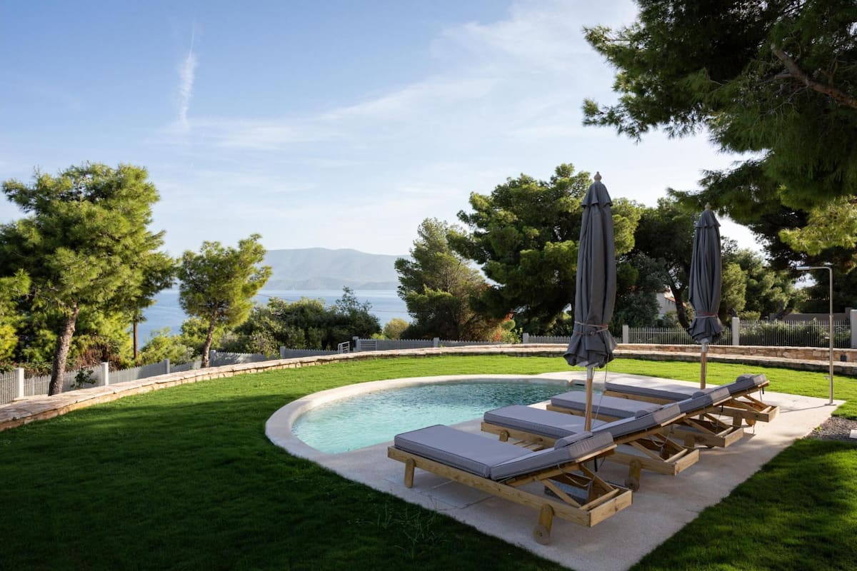 A swimming pool with lounge chairs and umbrellas, surrounded by a well-maintained lawn and trees.