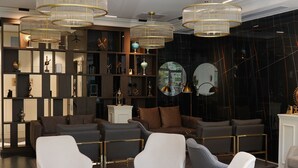 Un lobby moderno con una zona de estar central, suelo a cuadros blanco y negro y un espejo grande en la pared.