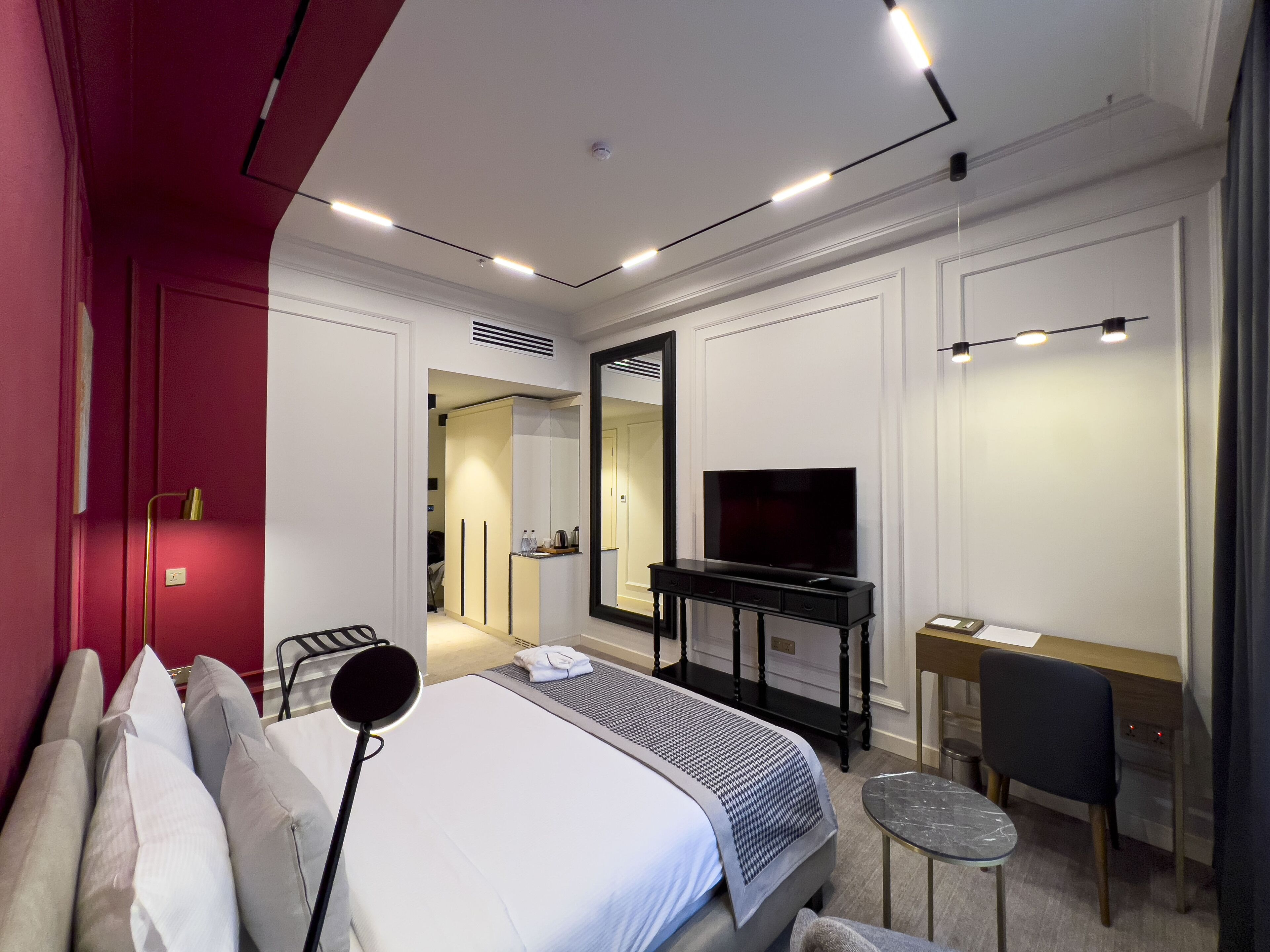 A modern hotel room with a bed, bedside table, TV, desk, chair, and a mirror.