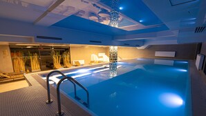 Una piscina interior con superficie de agua cristalina, una escalera metálica y un techo con iluminación empotrada.